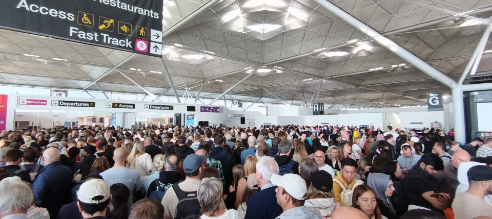 Large crowd of people at a UK airport experiencing flight delays due to an IT issue.