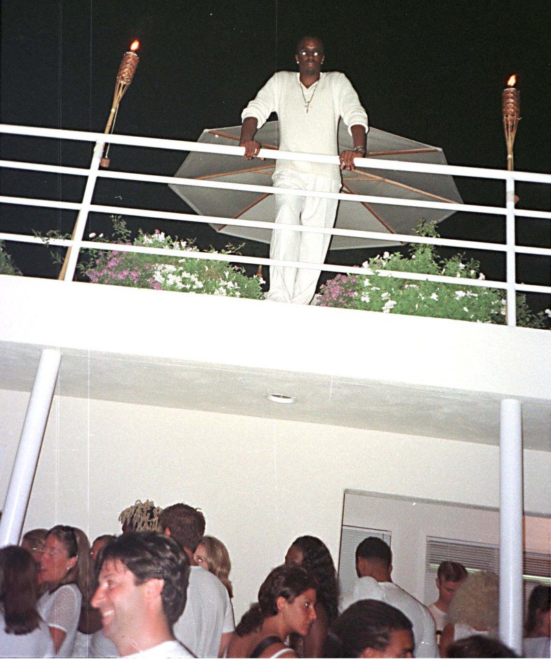 A man in white clothing stands on a balcony overlooking a party.