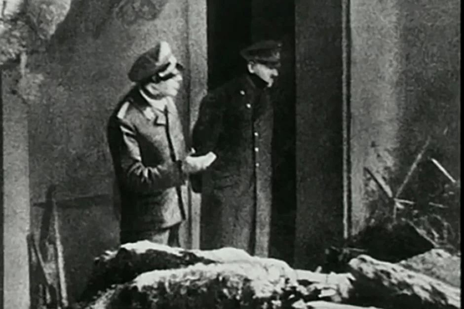 Black and white photo of two men in uniform standing near a pile of bodies.
