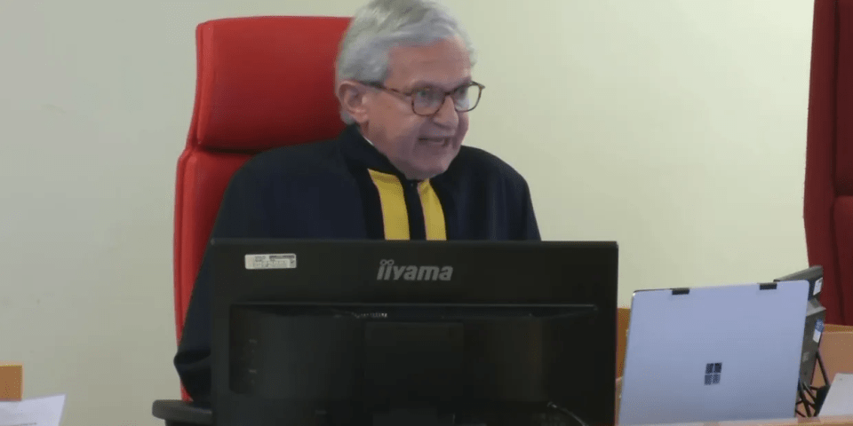Judge sitting at a desk with a computer and laptop.