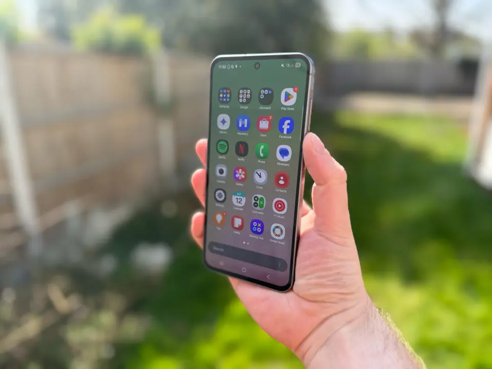 Hand holding smartphone displaying various app icons.