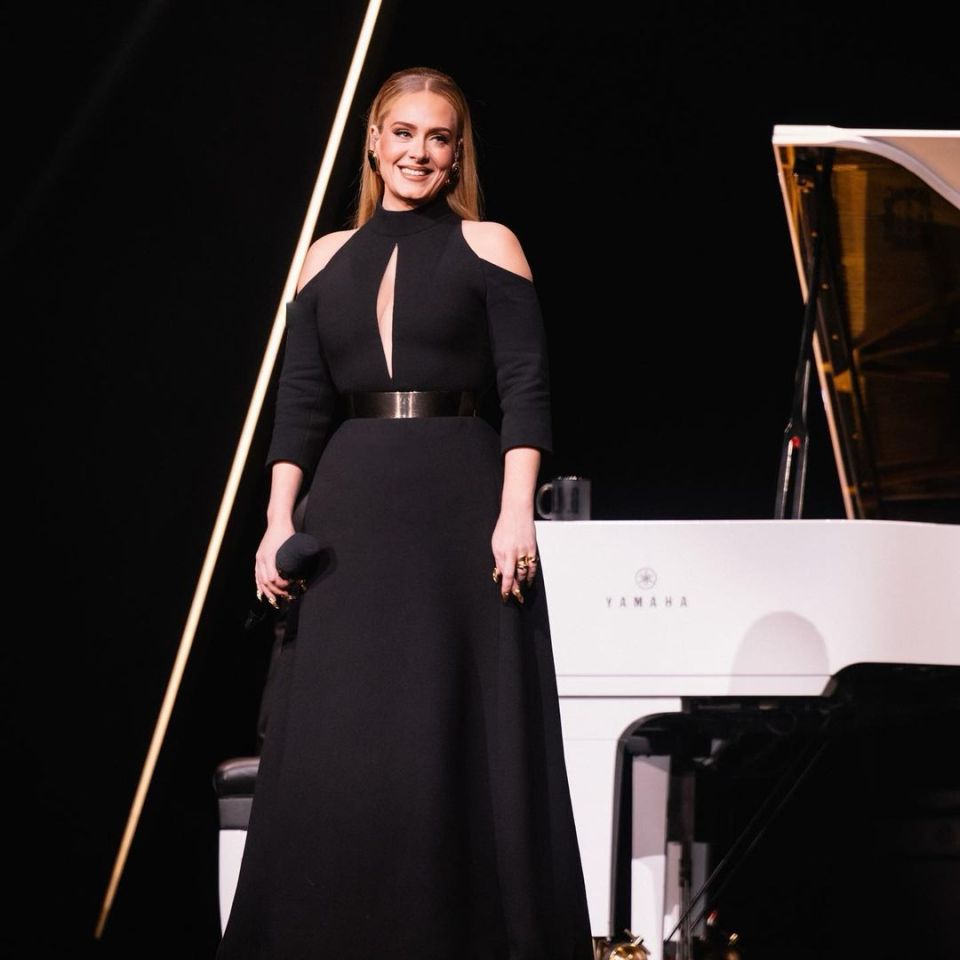 Adele holding a microphone on stage in front of a white piano.