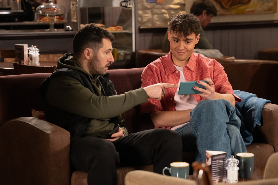 Two men sitting on a couch looking at a smartphone.