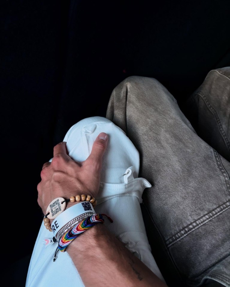 Close-up of a person's hand resting on another person's lap; the hand is adorned with several bracelets.