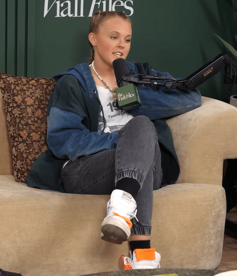 Woman sitting on a couch, speaking into a microphone.
