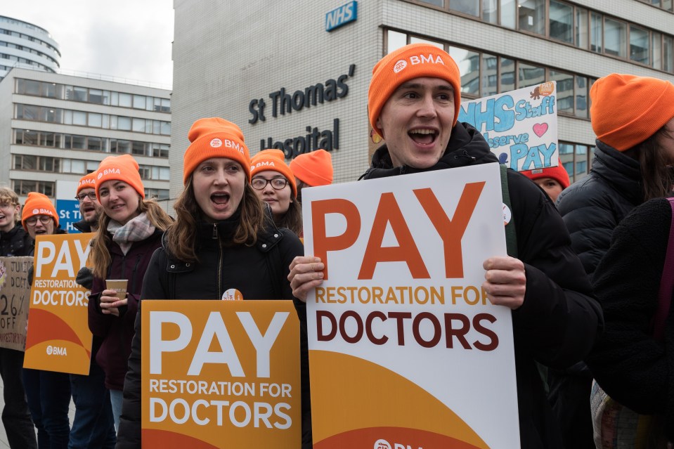 Junior doctors on picket line holding signs that read "Pay Restoration for Doctors."