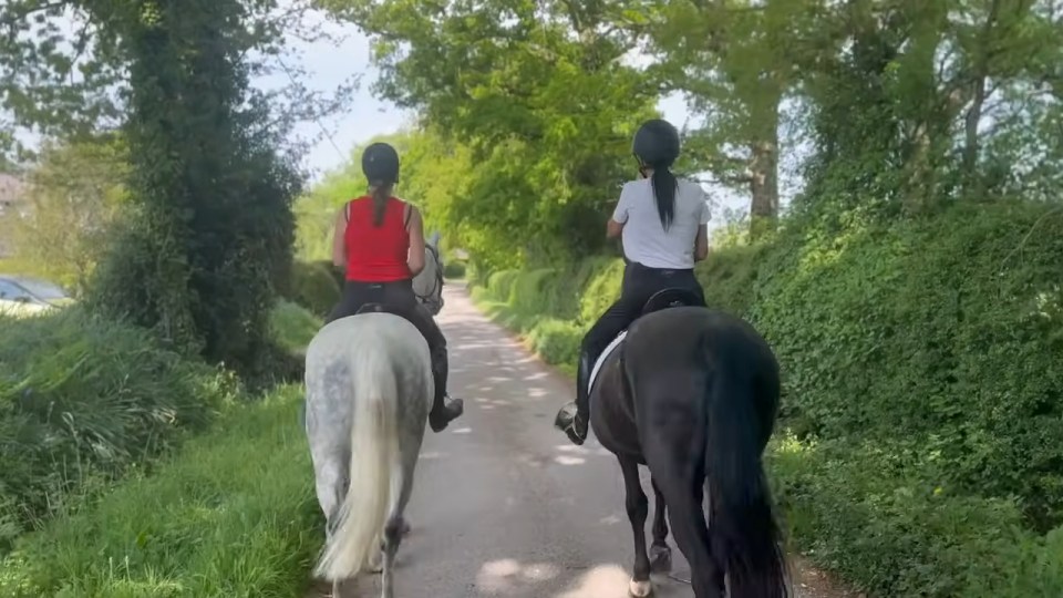 Two women horseback riding down a country lane.