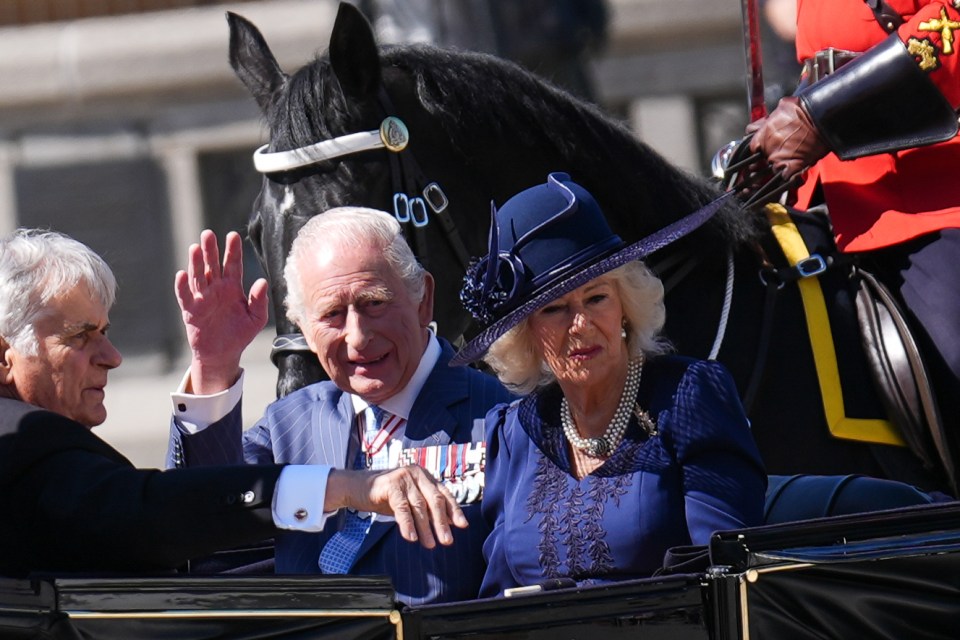 King Charles III and Queen Camilla waving from a carriage.