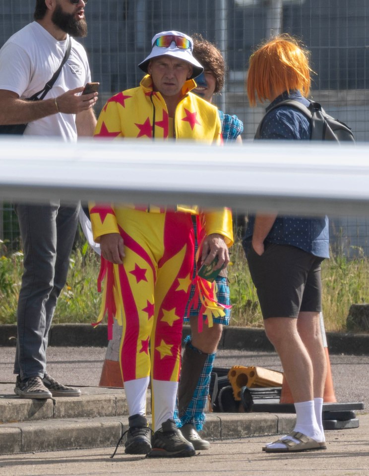 A man in a yellow and red star-patterned jumpsuit boards a private jet with friends.