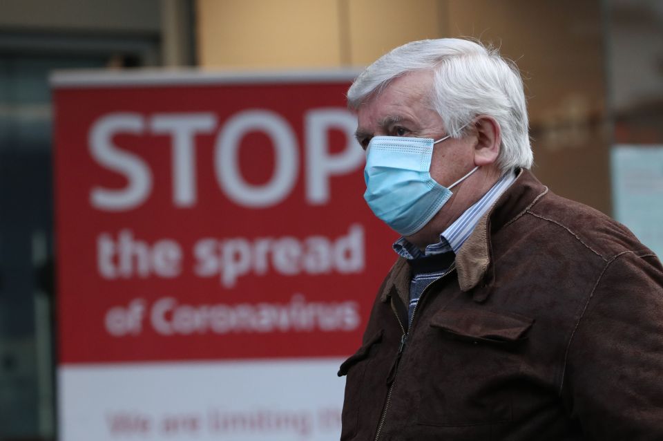 Man wearing a face mask walks past a sign that says "Stop the spread of Coronavirus".