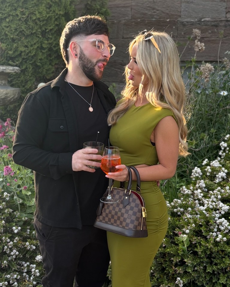 A man and woman playfully sticking out their tongues while holding drinks.