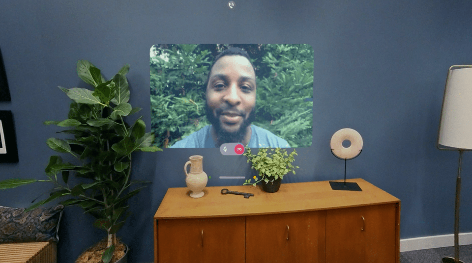 Video call displayed on a wall, with a man visible in the video.