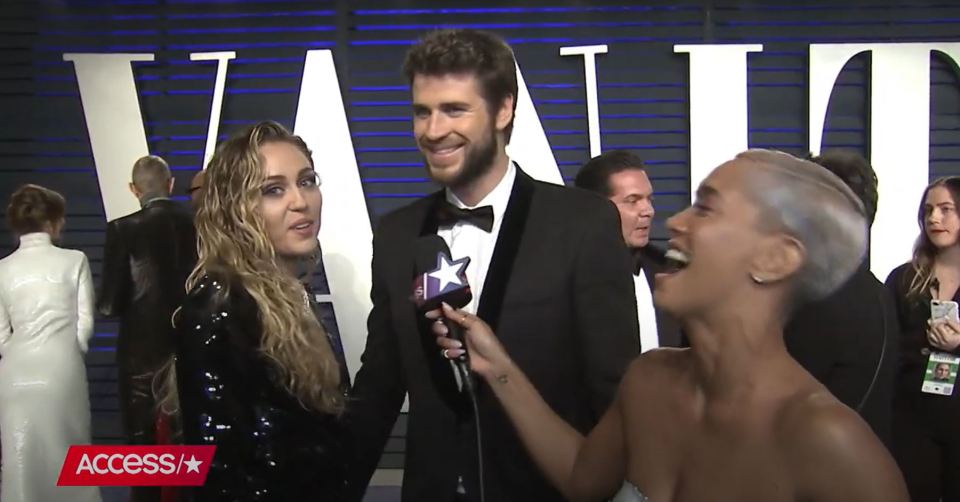Miley Cyrus and Liam Hemsworth being interviewed on a red carpet.
