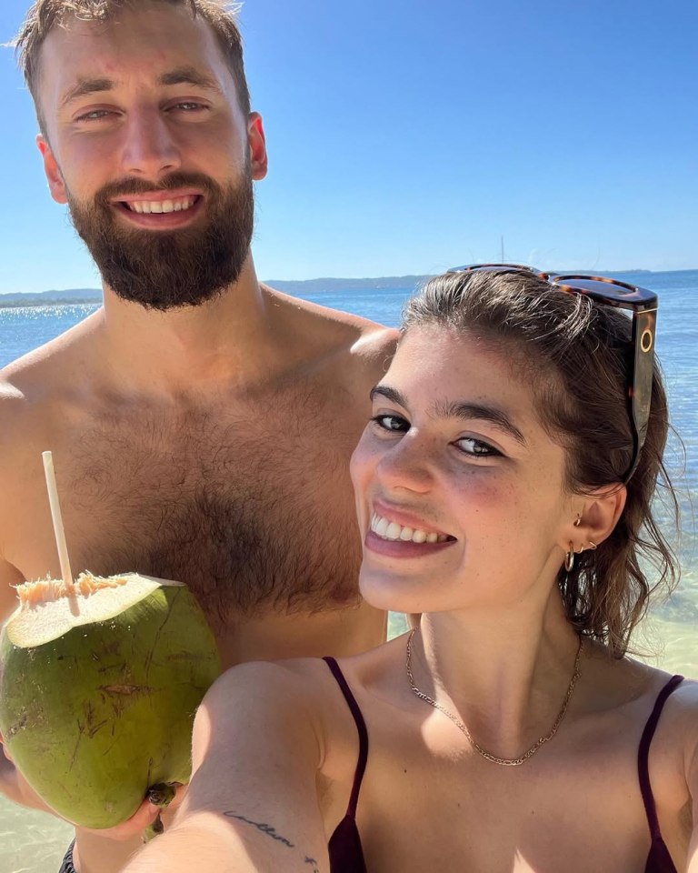 Molly Gallagher pregnant, at the beach with a man, holding a coconut.