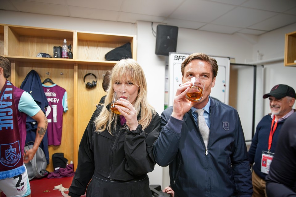 Natasha Bedingfield and a man drinking whiskey in a football club locker room.