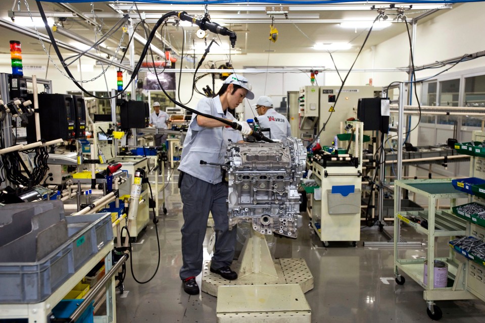 Nissan employee assembling a car engine on a factory production line.