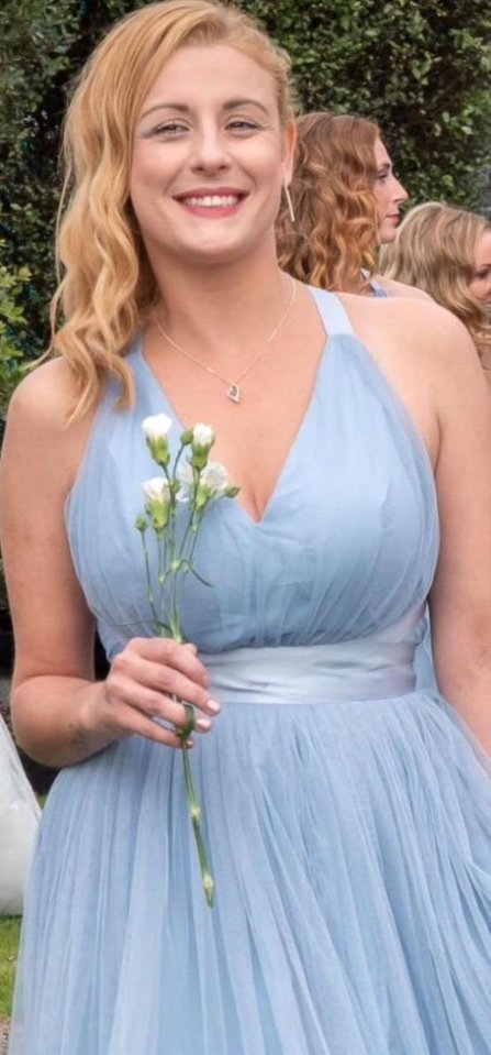 Photo of a young woman in a light blue bridesmaid dress holding a small bouquet of white flowers.