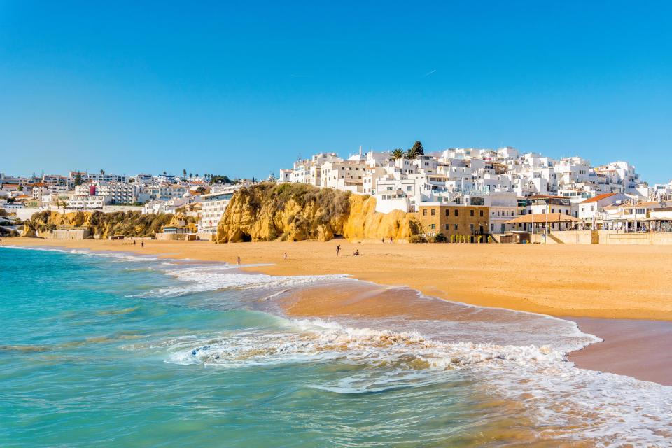 Sandy beach with ocean waves and whitewashed buildings in Albufeira, Portugal.
