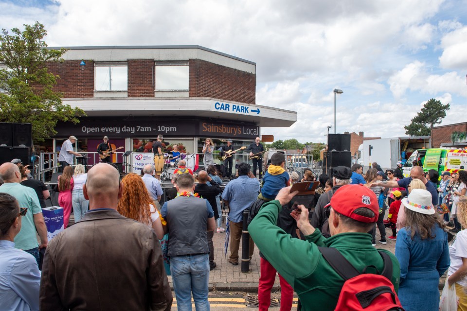 Crowd at an outdoor concert in front of a Sainsbury's Local.
