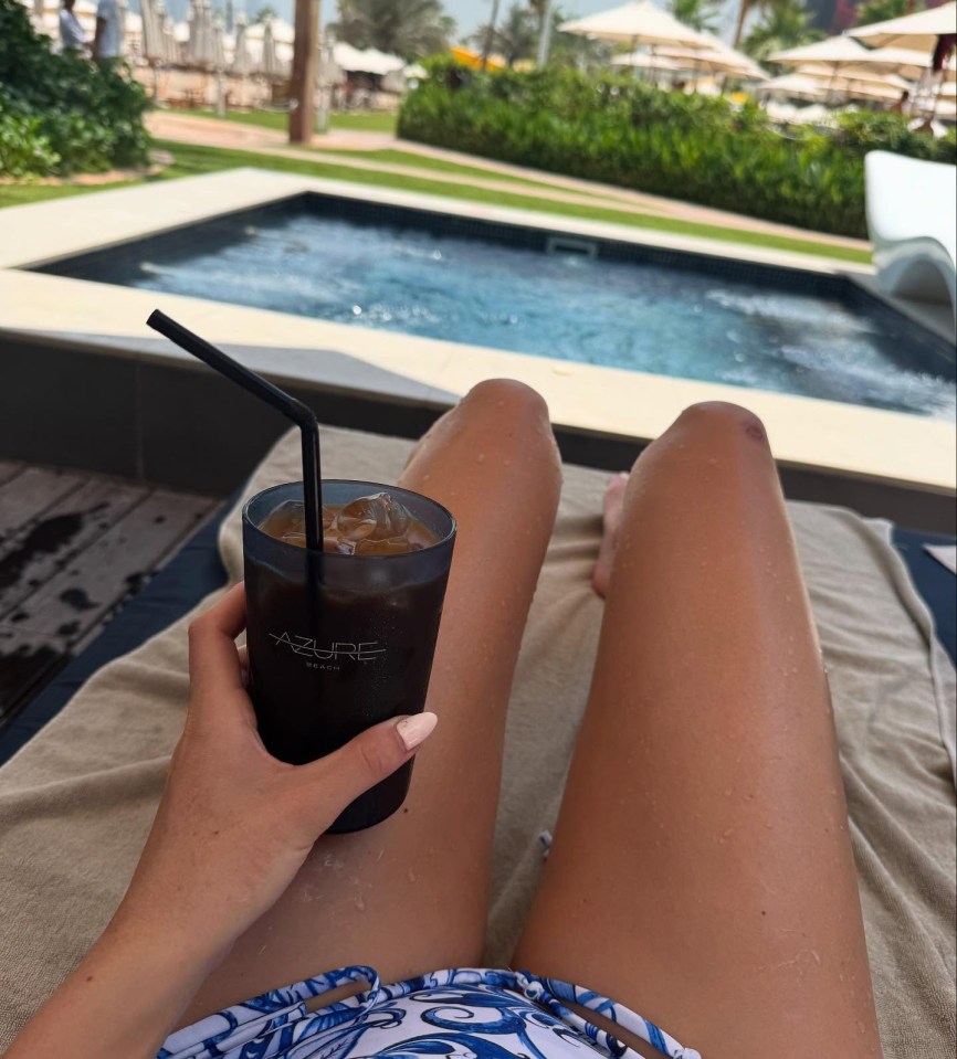 Person relaxing by a pool with an iced coffee.