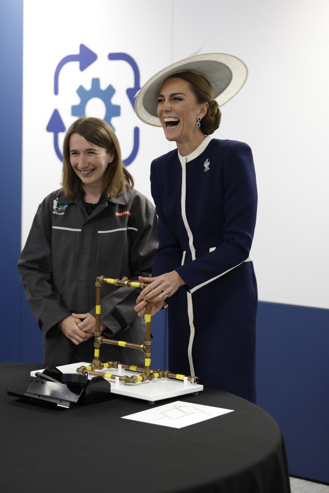 The Princess of Wales and another woman laughing while looking at a model made of copper pipes.
