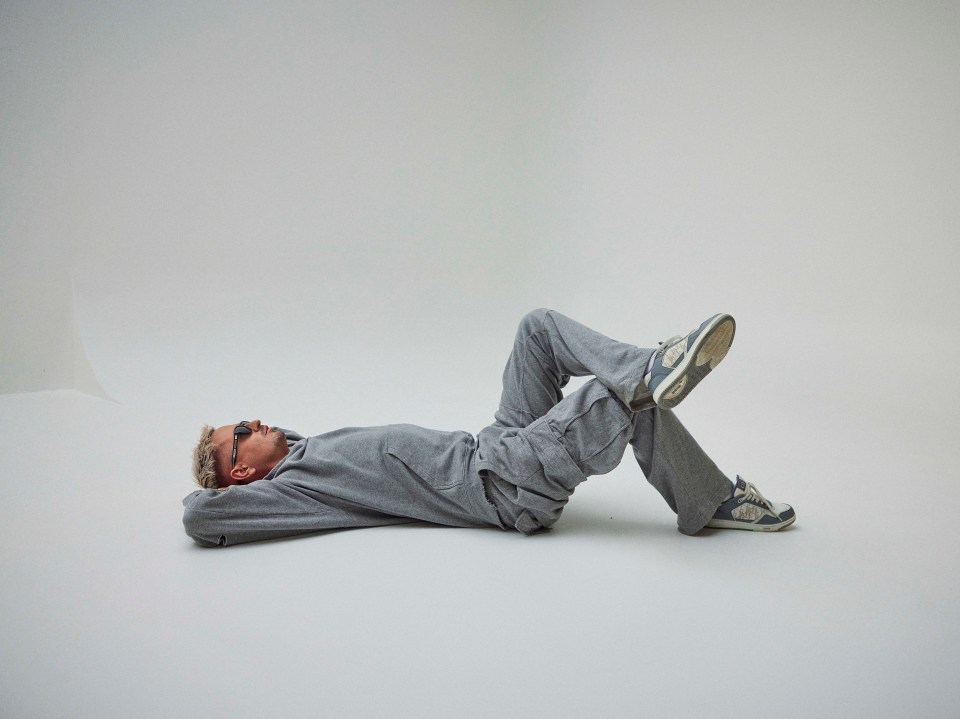 Man wearing gray sweatsuit lying on the floor.