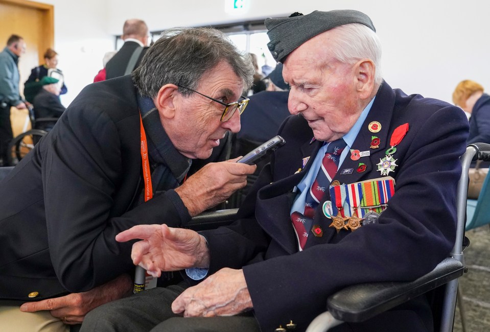 A reporter interviews a veteran in a wheelchair at a VE Day anniversary event.