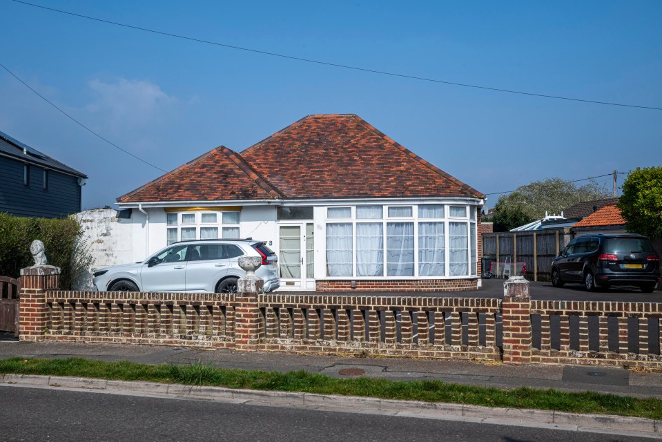 A bungalow with a red tile roof and a large bay window.  A silver SUV is parked in front.