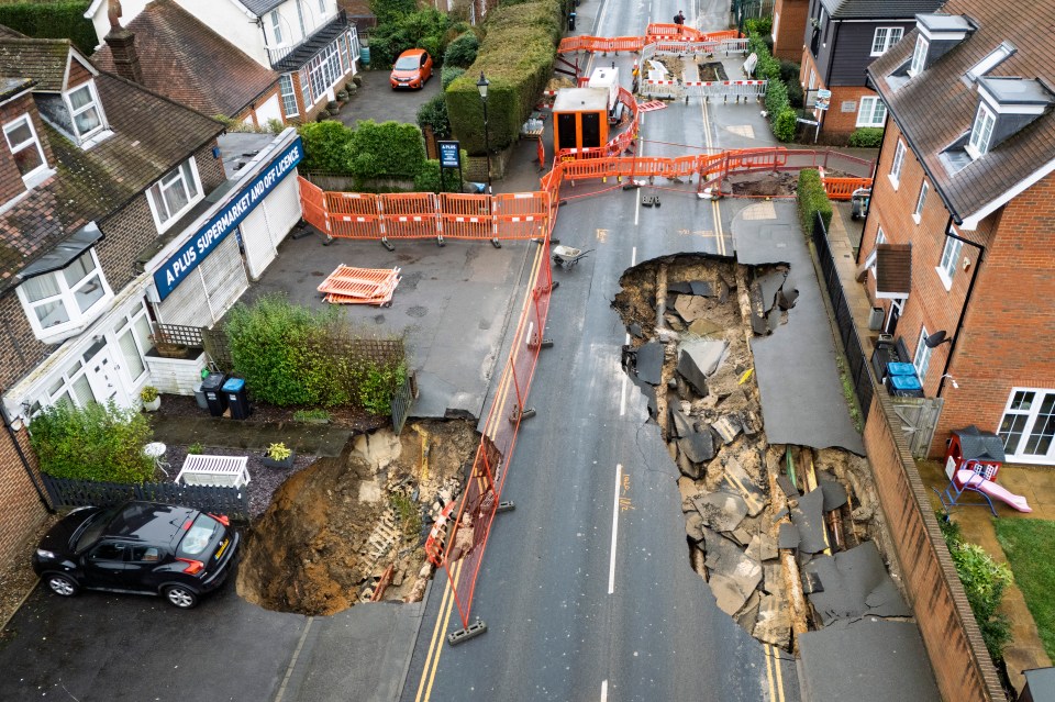 Aerial view of two large sinkholes in a residential street, surrounded by safety barriers.