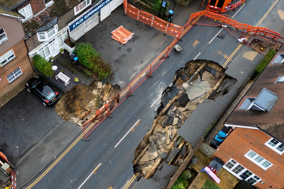 Aerial view of two sinkholes in a road, surrounded by safety barriers.