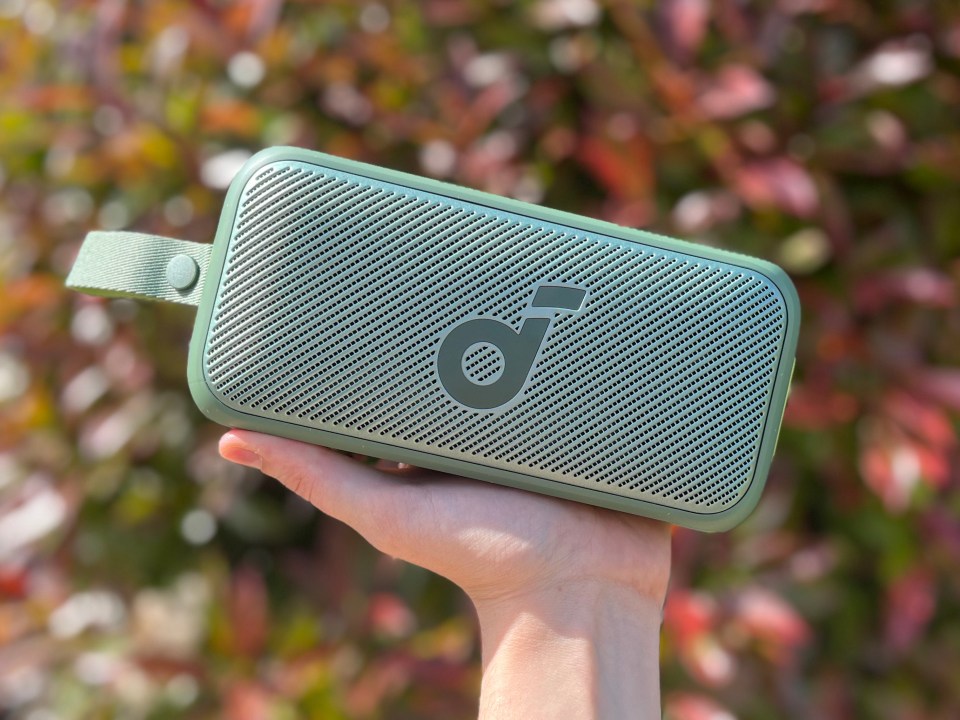 A hand holding a green Soundcore Motion 300 portable speaker.