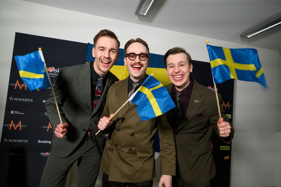 Three men in suits celebrating with Swedish flags.