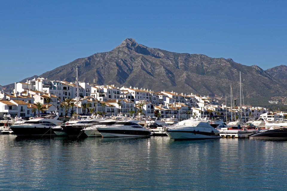 Puerto Banus marina with yachts and white buildings against a mountain backdrop.