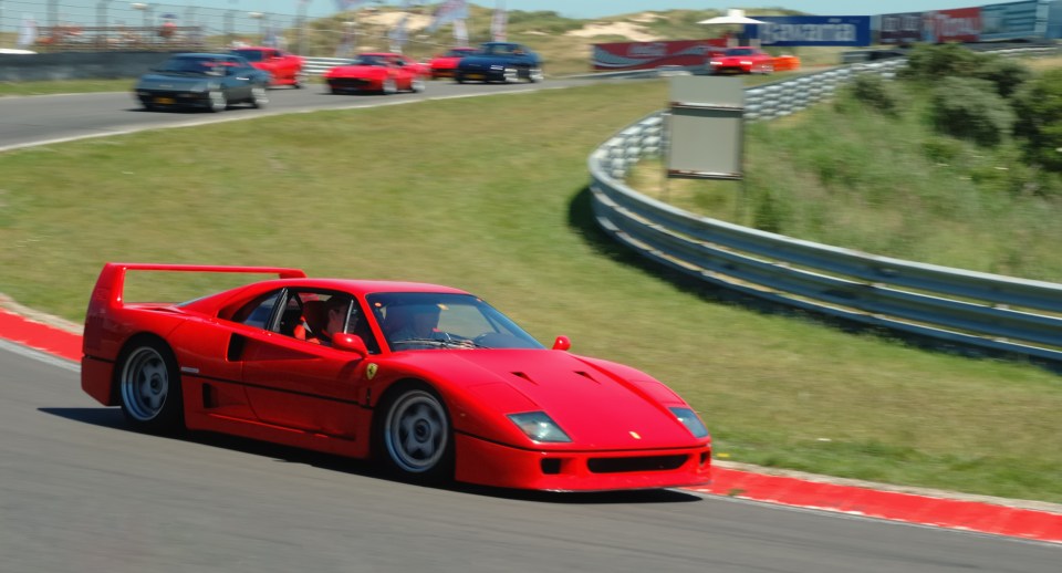 Red Ferrari F40 driven by two men on a racetrack.