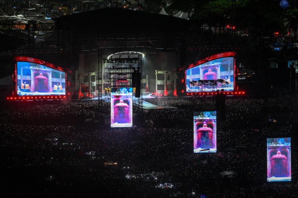 Lady Gaga performing on stage at a concert with large screens showing her image.