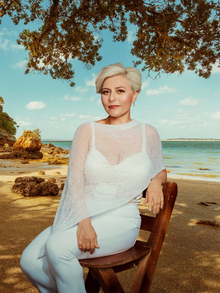 Woman in white sitting on a bench by the beach.