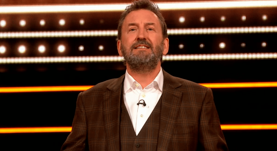 Man in brown suit on game show set.