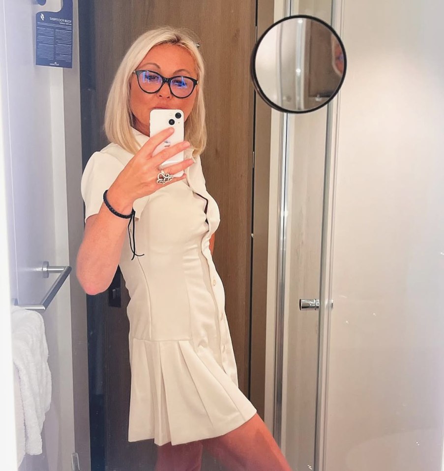 Woman in a white dress taking a selfie in a bathroom.