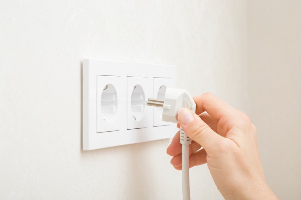 A hand plugging a white electrical plug into a wall outlet.