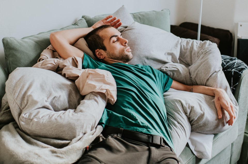 Man sleeping on a couch surrounded by pillows.
