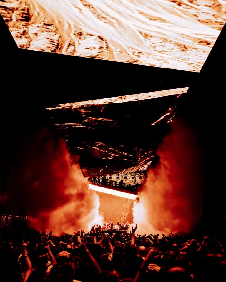 Concert crowd with performers on stage and large screens overhead.