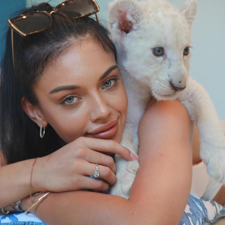 Woman with a white lion cub on her shoulder.