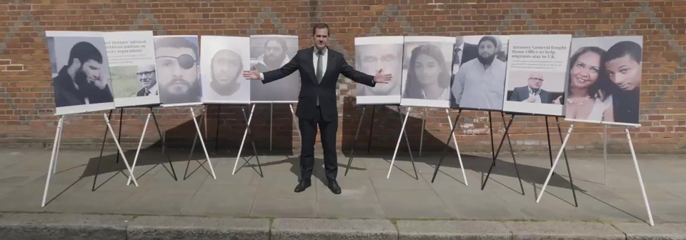 A man in a suit stands before several portrait displays of various individuals.