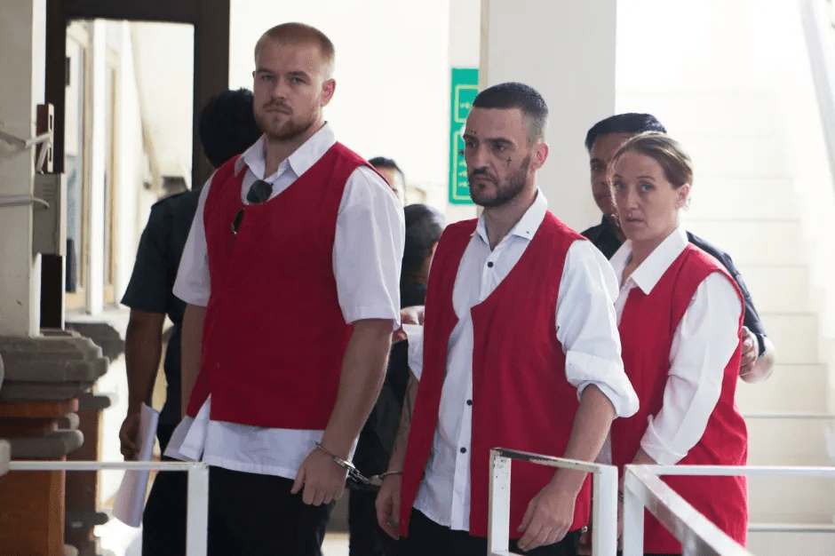 Three people in red vests and handcuffs.