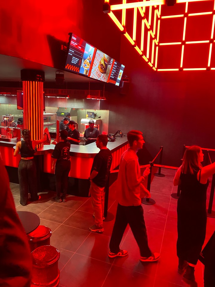 Customers ordering food at a concession stand with red lighting.