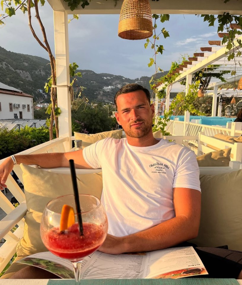 Man sitting outdoors at a restaurant with a drink and menu.