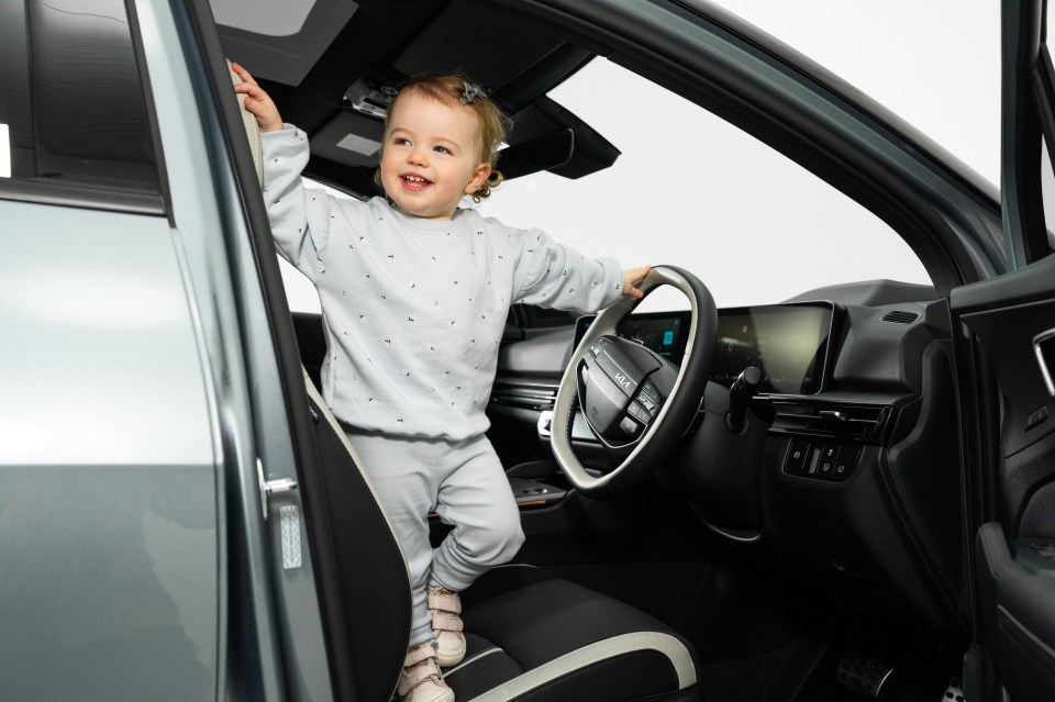 Toddler in car, holding steering wheel.