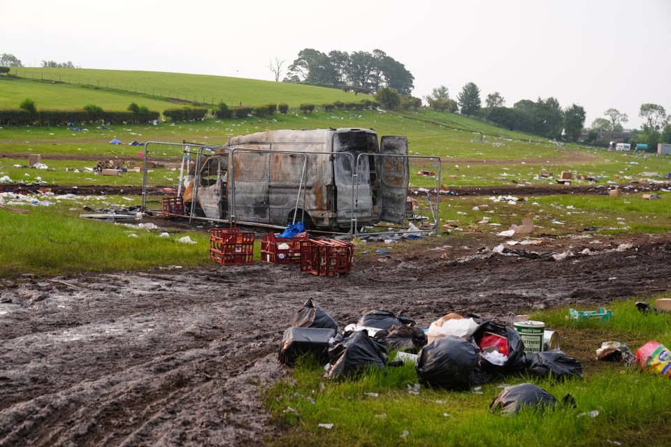Burned-out van surrounded by trash in a field.